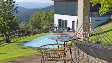 Zona de piscina con mobiliario exterior y una hamaca, con vistas a un paisaje montañoso.