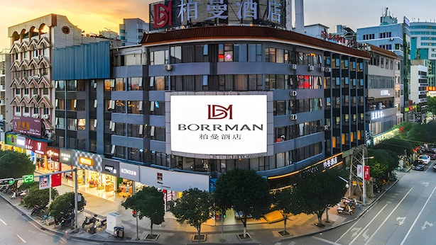 A multi-story building with a prominent Borman hotel sign, surrounded by other commercial buildings and a busy street. - Borrman Hotel (Hezhou)