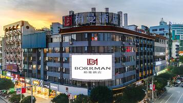 A multi-story building with a prominent Borman hotel sign, surrounded by other commercial buildings and a busy street.