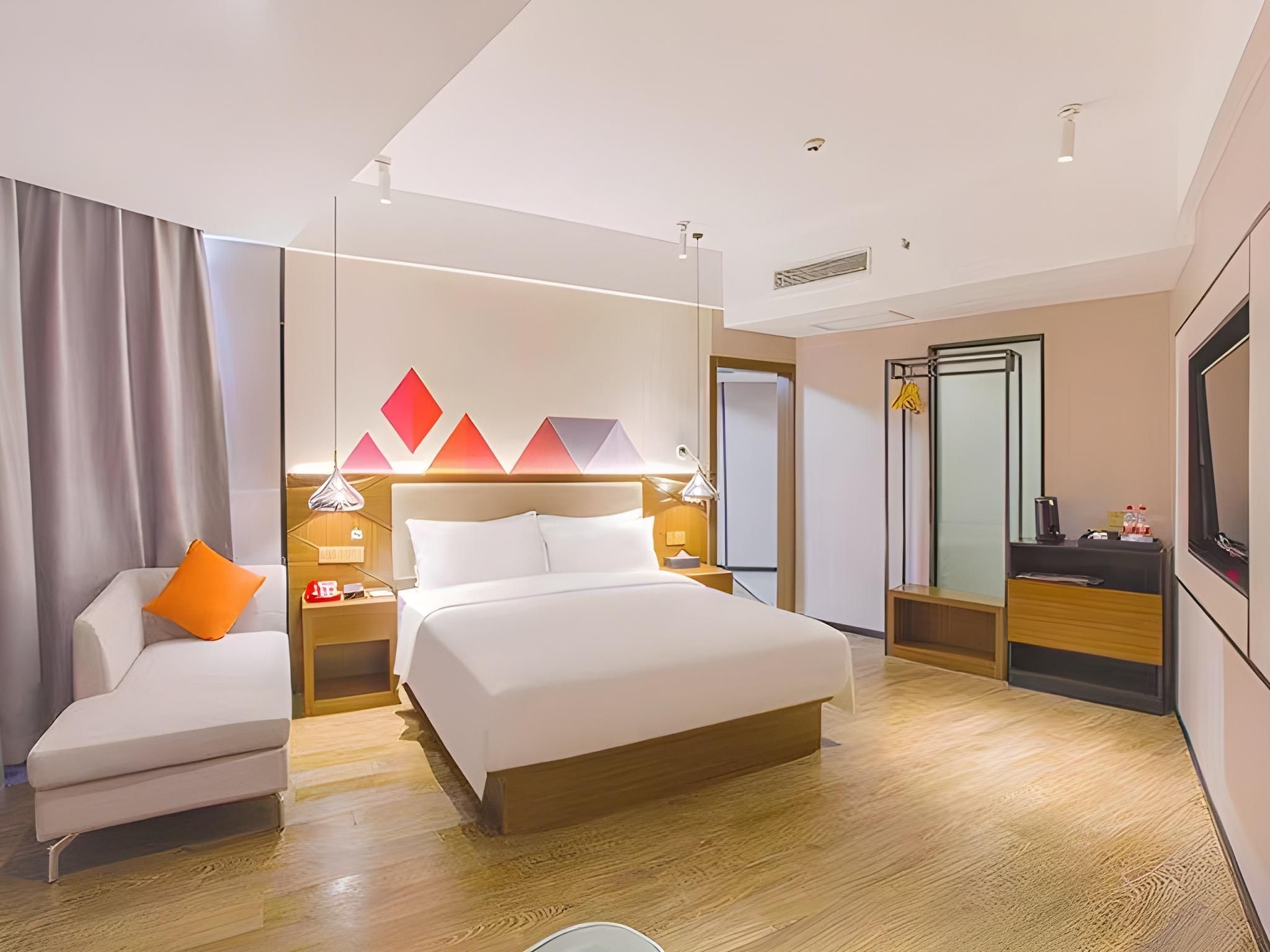 A modern hotel room with a bed, a sofa, a desk, and a mirror.