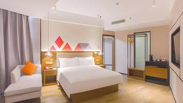 A modern hotel room with a bed, a sofa, a desk, and a mirror.
