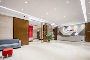 A modern hotel lobby with a reception desk, a seating area with a sofa and chairs, and a decorative plant.