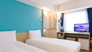 Et hotelværelse med to senge, et skrivebord med en computer, et fjernsyn og et vindue med gardiner.