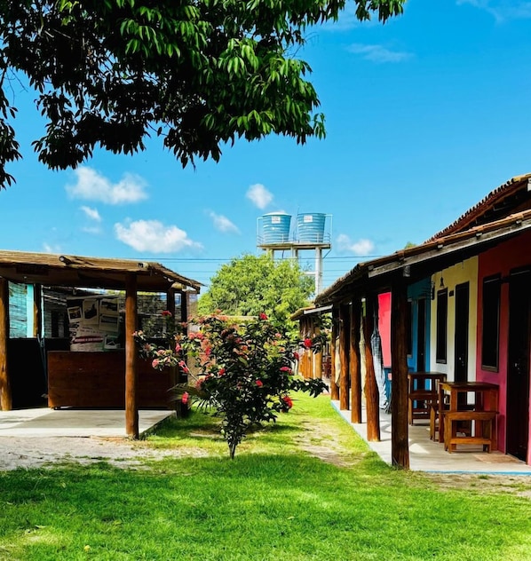 A courtyard with a water tower, wooden structures, and a small tree with pink flowers. - Pousada Aquarela Caraiva (Porto Seguro)