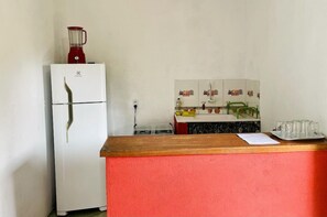 A kitchen with a white refrigerator, a red blender on top, a wooden counter, and a tiled backsplash. - Pousada Aquarela Caraiva (Porto Seguro)