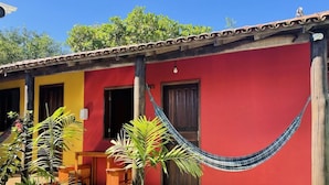 A red building with a porch, a hammock, and a small garden. - Pousada Aquarela Caraiva (Porto Seguro)