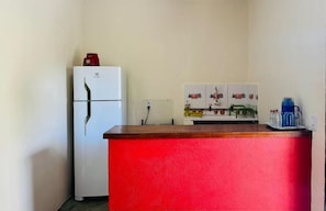 A compact kitchen with a white refrigerator, a red countertop, and a wall-mounted sink. - Pousada Aquarela Caraiva (Porto Seguro)