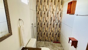 A bathroom with a shower, toilet, sink, and a mirror. - Pousada Aquarela Caraiva (Porto Seguro)