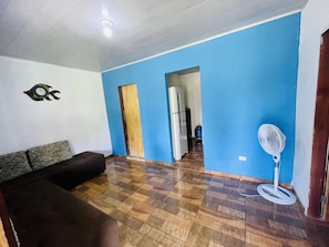 A room with a brown sofa, a white fan, and a blue wall. - Pousada Aquarela Caraiva (Porto Seguro)