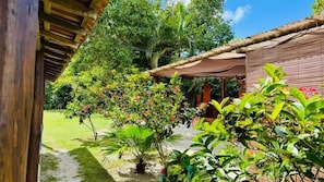 A covered outdoor area with a wooden structure, surrounded by lush greenery and flowering plants. - Pousada Aquarela Caraiva (Porto Seguro)