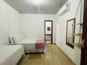 A small, single-room accommodation with a bed, a bedside table, a mirror, and a shelf. - Pousada Aquarela Caraiva (Porto Seguro)