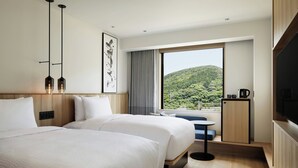 Ein Hotelzimmer mit zwei Betten, einem großen Fenster mit Bergblick, einem Flachbildfernseher und einem kleinen Tisch mit Wasserkocher.
