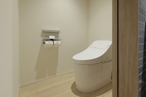Et moderne badeværelse med toilet, papirhåndklædedispenser og trægulv.