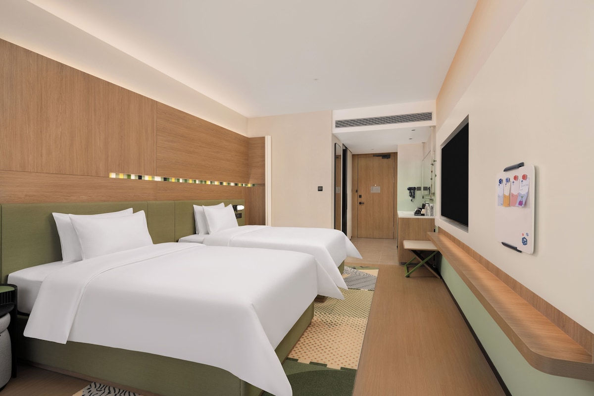 A hotel room with two beds, a desk, a mirror, and a TV.