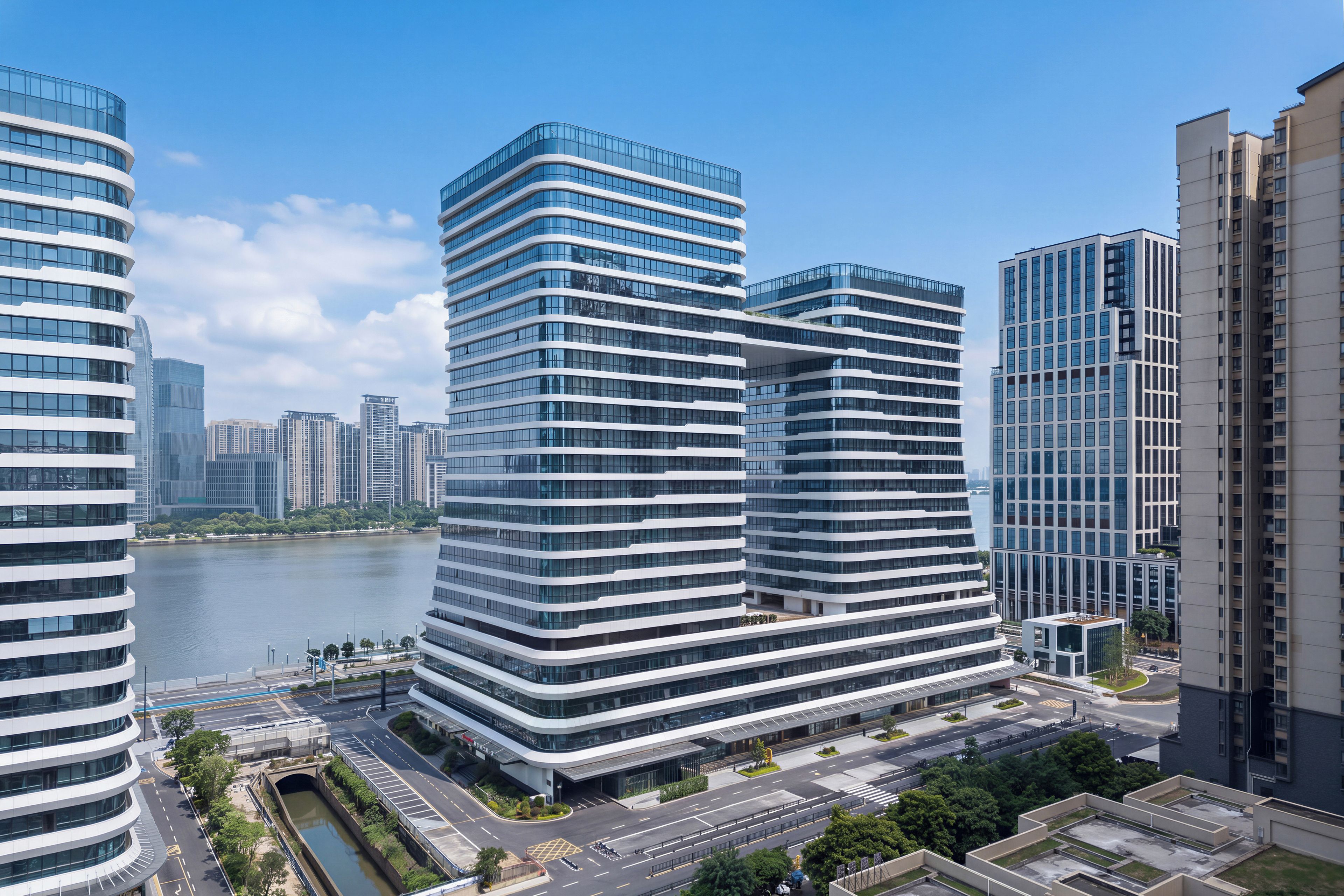 A modern high-rise building with a curved facade, surrounded by other high-rise buildings and a body of water.
