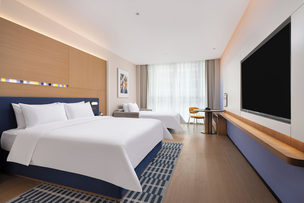 A hotel room with a large bed, a desk, a chair, and a TV.
