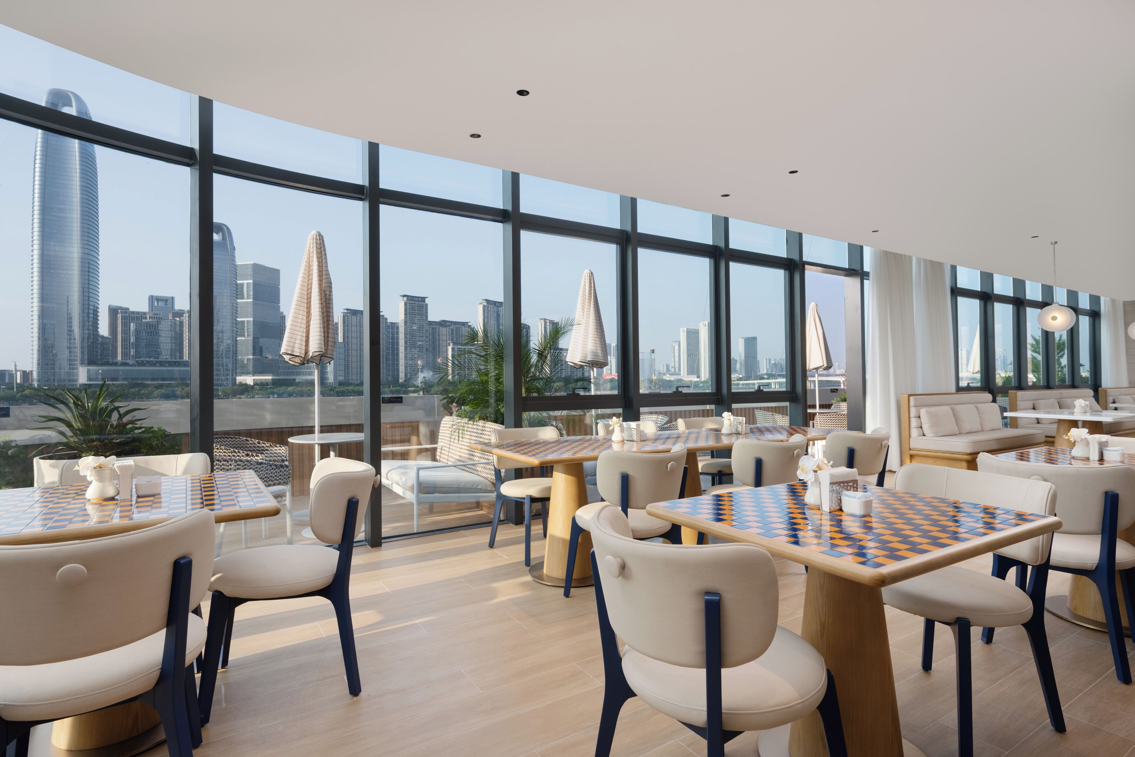 Un espace repas moderne doté de grandes fenêtres, offrant une vue sur la ville, et comprenant des tables d’échecs.