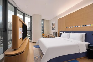 A hotel room with a bed, a TV, a desk, and a view of the city. - Hampton Apartments by Hilton Guangzhou Financial City Linjiang Avenue (Guangzhou, Tianhe District)