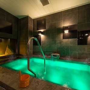 Un espace détente avec un jacuzzi éclairé de lumière verte, une échelle en métal et un petit tabouret en bois.