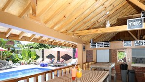 An outdoor bar area with wooden tables and benches, a pool, and a sign indicating a 'crew driver' service. - Toba Village Inn (Samosir)