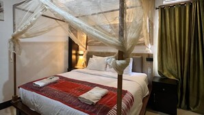 A four-poster bed with a canopy, a bedside table, a lamp, and a green curtain. - Toba Village Inn (Samosir)