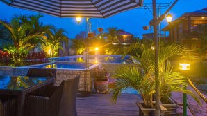 Un área junto a la piscina con una silla de descanso, una sombrilla a rayas y una piscina bien iluminada.