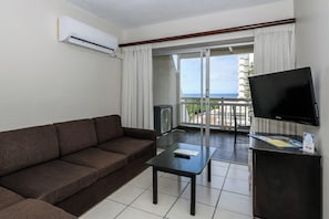A hotel room with a sofa, a television, a small table, and a balcony with a view of the sea. - Umhlanga Cabanas (uMhlanga)