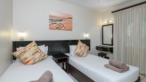 Camera d'albergo con due letti, un comodino, uno specchio e un quadro raffigurante una spiaggia.
