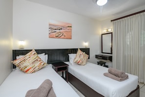 A hotel room with two beds, a nightstand, a mirror, and a painting of a beach scene. - Umhlanga Cabanas (uMhlanga)