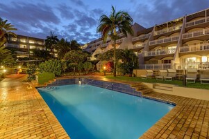 Un hotel con piscina, palmeras y un camino de ladrillo.