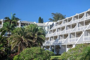 Un hotel con varios balcones y un exuberante jardín con palmeras.