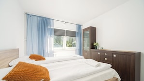 A bedroom with a bed, two pillows, a dresser, and a window with curtains. - RentPlanet - Apartament Górczewska (Warszawa)