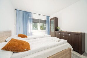 Un dormitorio con cama, dos almohadas, cómoda y ventana con cortinas.