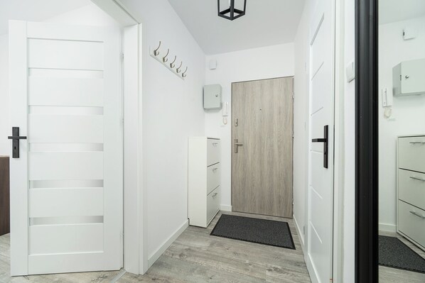 A hallway with a white door, a wooden door, and a white cabinet. - RentPlanet - Apartament Górczewska (Warszawa)
