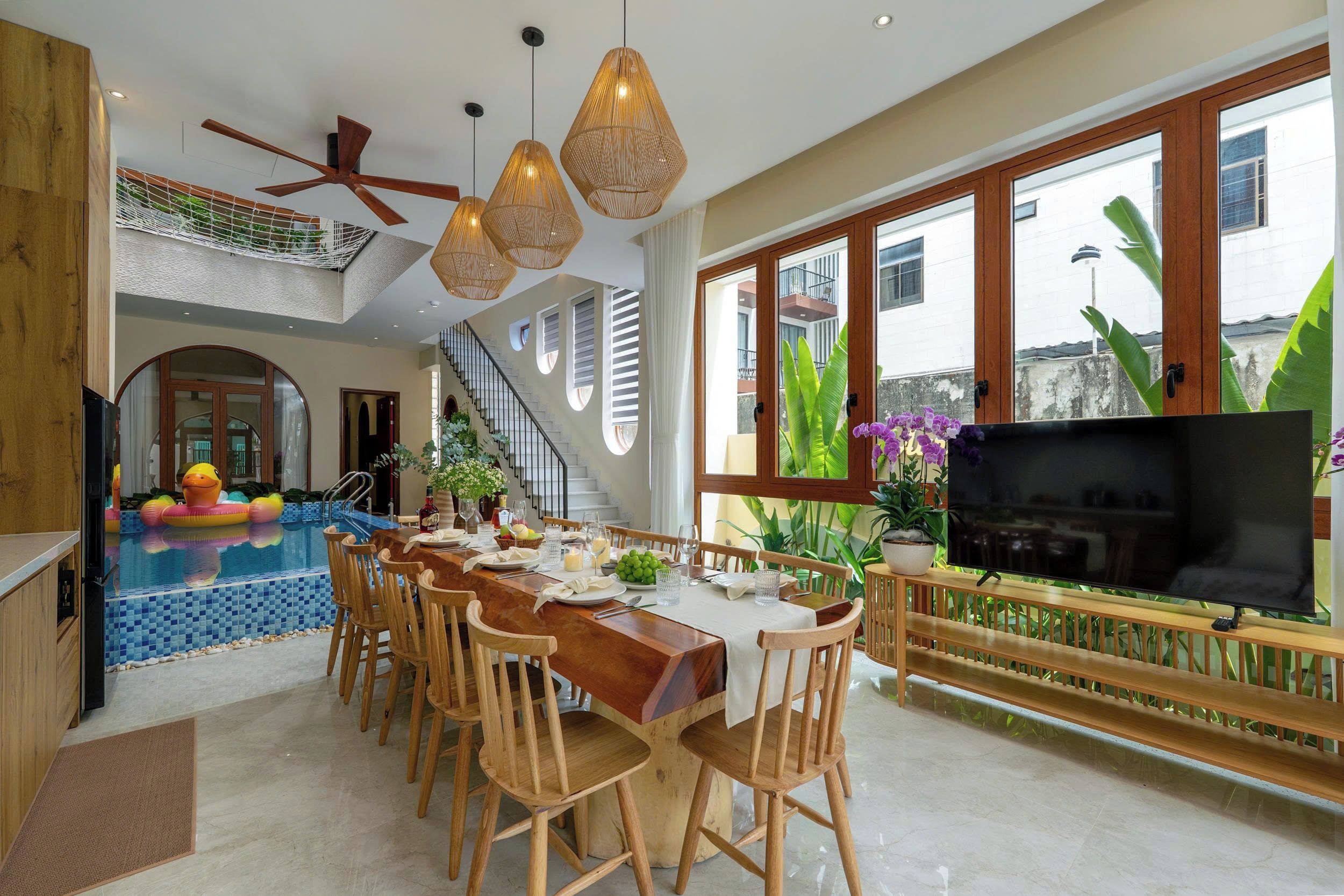 A spacious dining area with a pool, wooden furniture, and large windows.