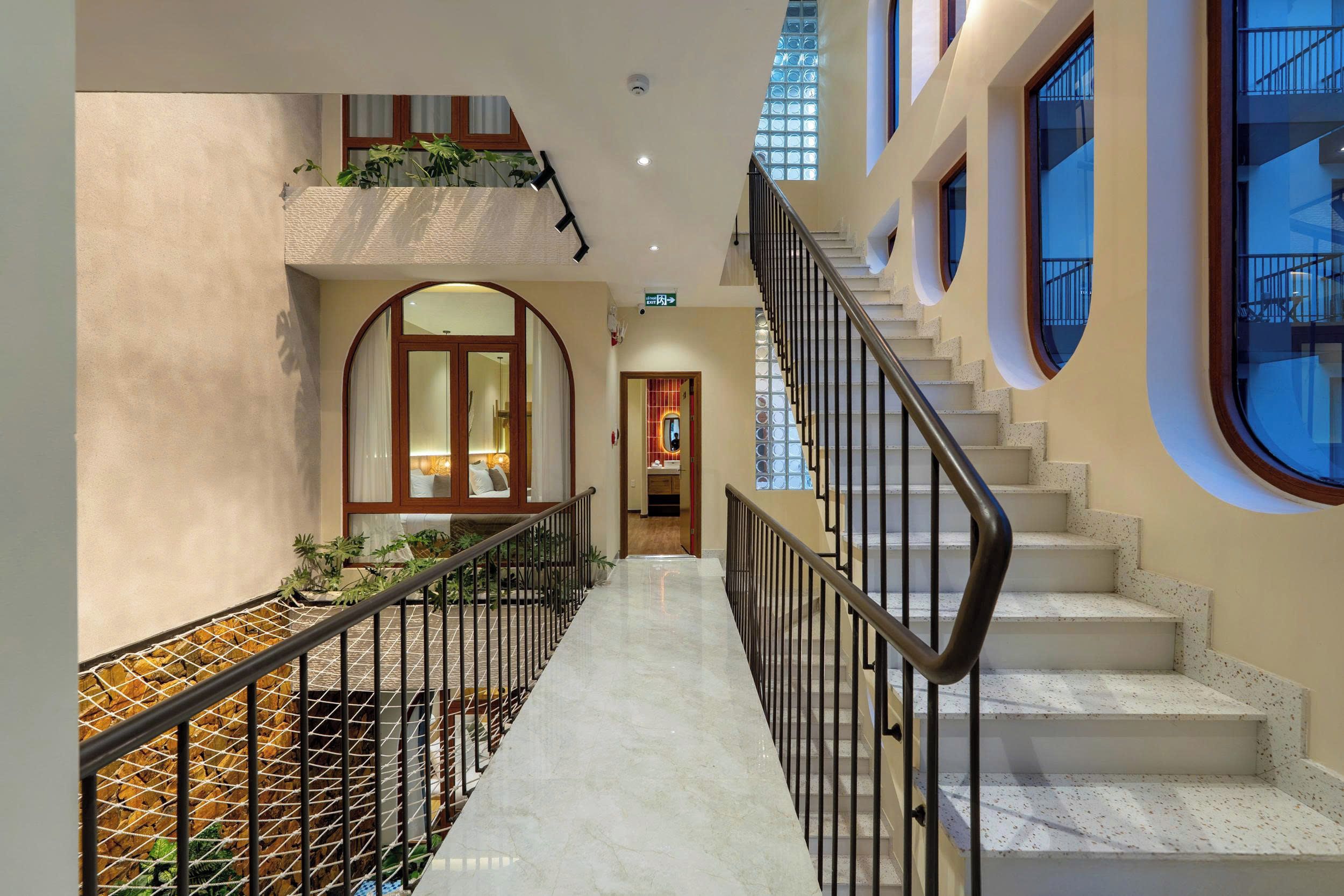 A corridor with a marble floor, a staircase with a metal railing, and a view of a room with a bed and a window.
