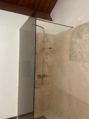 Et brusebad med glasvægge, metalramme, beige flisevægge og træloft.