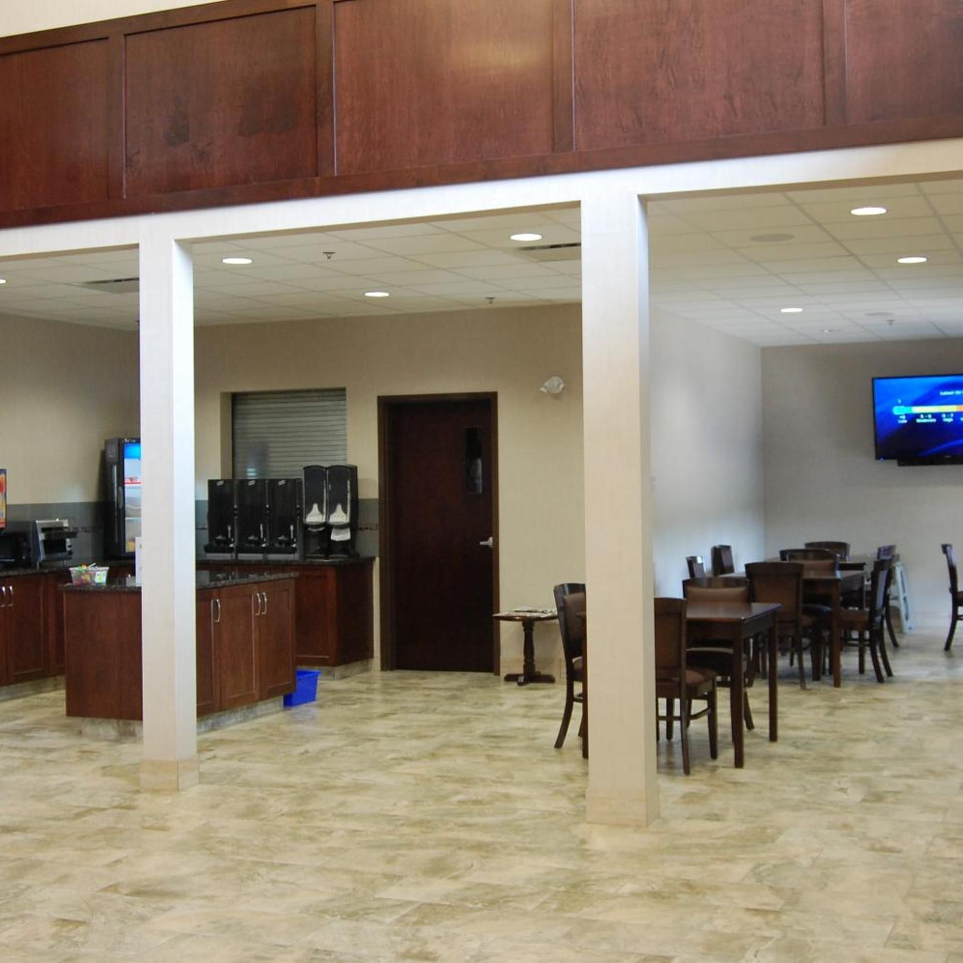 A hotel lobby with a coffee station, seating area, and a television mounted on the wall.
