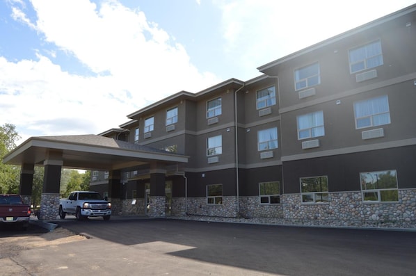 Ein mehrgeschossiges Hotel mit überdachter Eingangszone und Parkplatz.