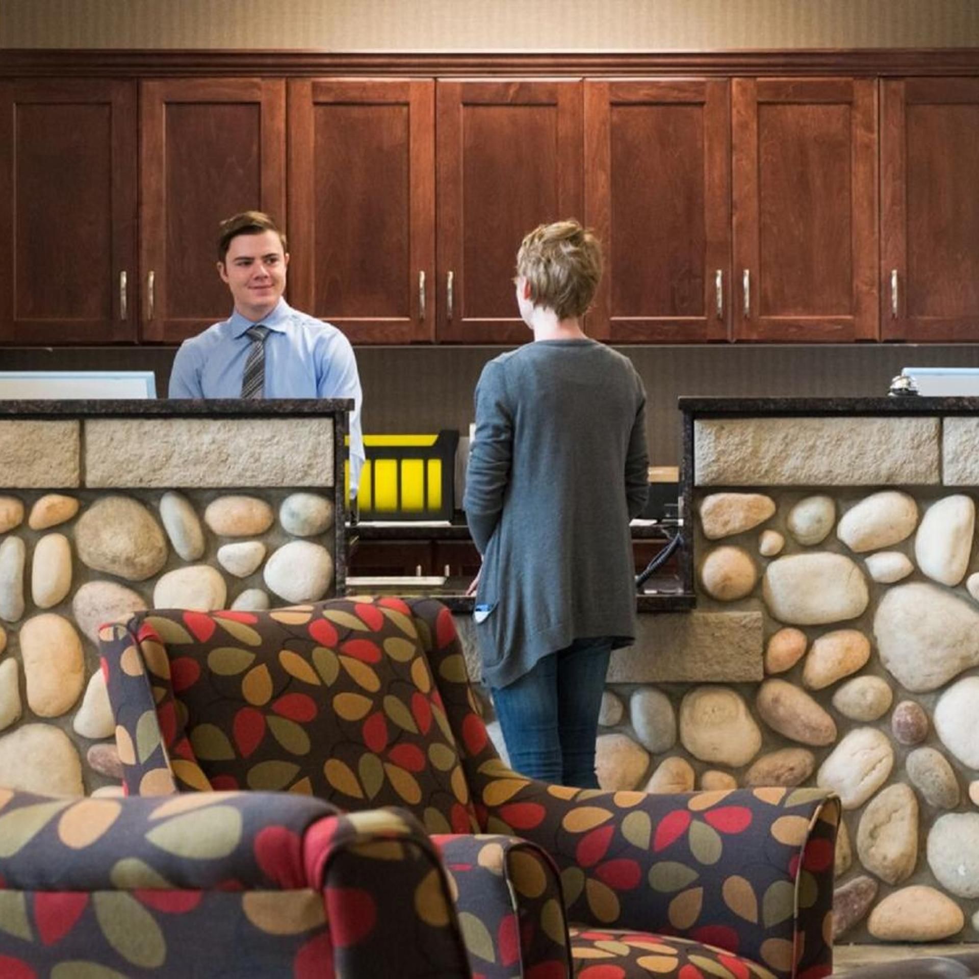 A reception area with a stone wall, wooden cabinets, and patterned armchairs.