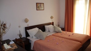 Habitación de hotel con dos camas, una mesita de noche de madera, una mesa con una cesta y un cuadro colgado en la pared.