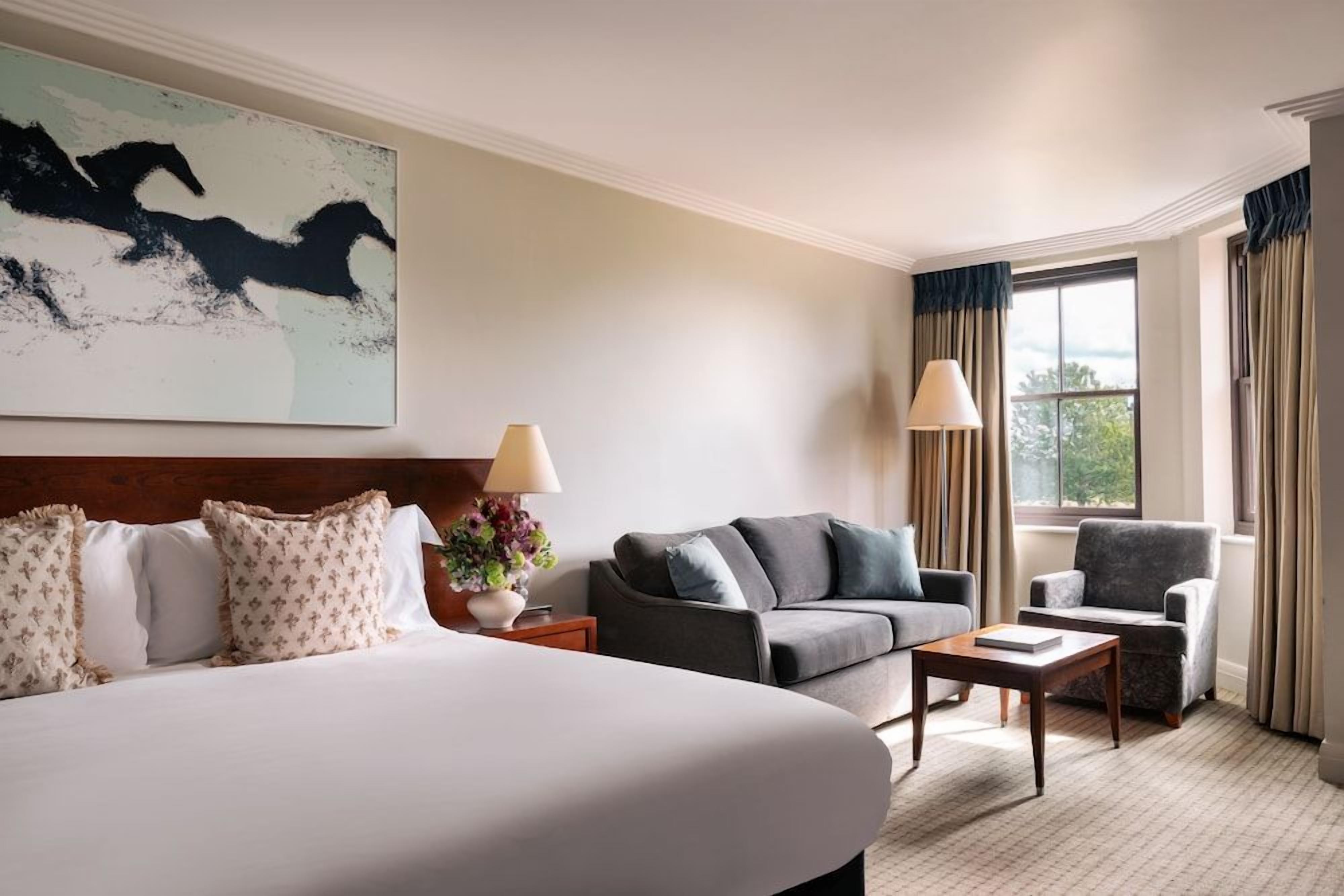 A hotel room with a large bed, a sofa, a chair, a small table, and a window with curtains.