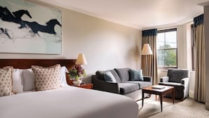 A hotel room with a large bed, a sofa, a chair, a small table, and a window with curtains.