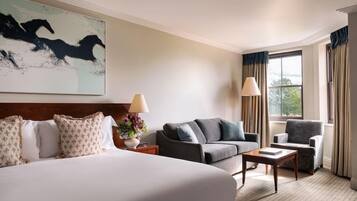 A hotel room with a large bed, a sofa, a chair, a small table, and a window with curtains.
