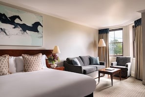 A hotel room with a large bed, a sofa, a chair, a small table, and a window with curtains.