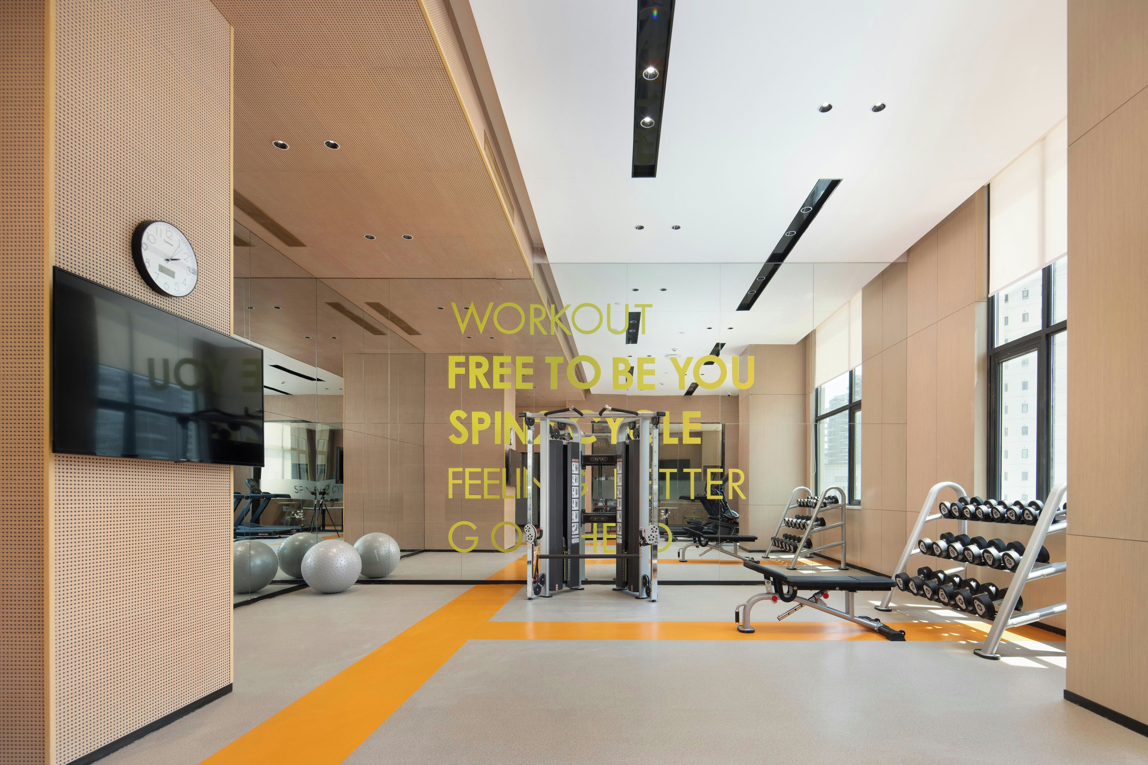 Een moderne sportschool met trainingsapparatuur, een klok en een groot raam.