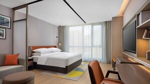 Una habitación de hotel con cama, escritorio, televisor y ventana con cortinas.
