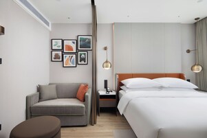 Habitación de hotel moderna con cama, sofá, mesita de noche y una pared con cuadros.
