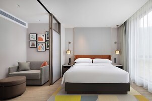 Una habitación de hotel moderna con una cama grande, un sofá, un escritorio y una pared con cuadros.