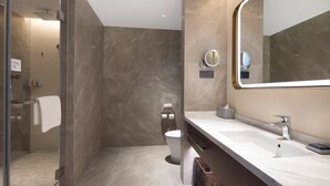 Un baño moderno con cabina de ducha de vidrio, un espejo grande y un lavamanos blanco.